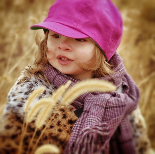 a girl in a pink hat is standing and holding onto some grass