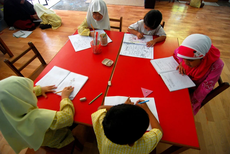 several children in yellow and green sitting at a table writing in their notebooks