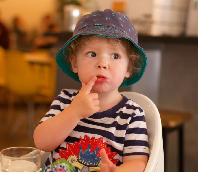 a boy sitting in a high chair with his finger in his mouth