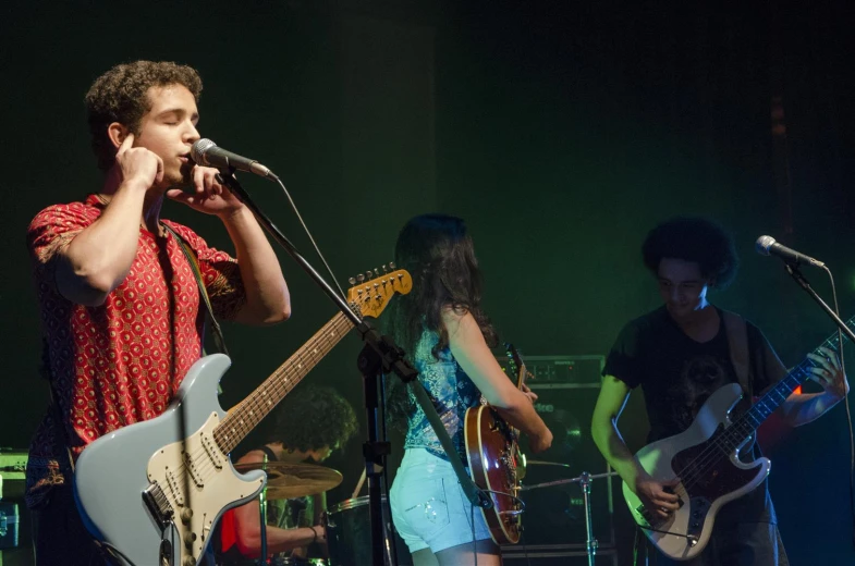 two people in front of microphones and guitar, one on stage