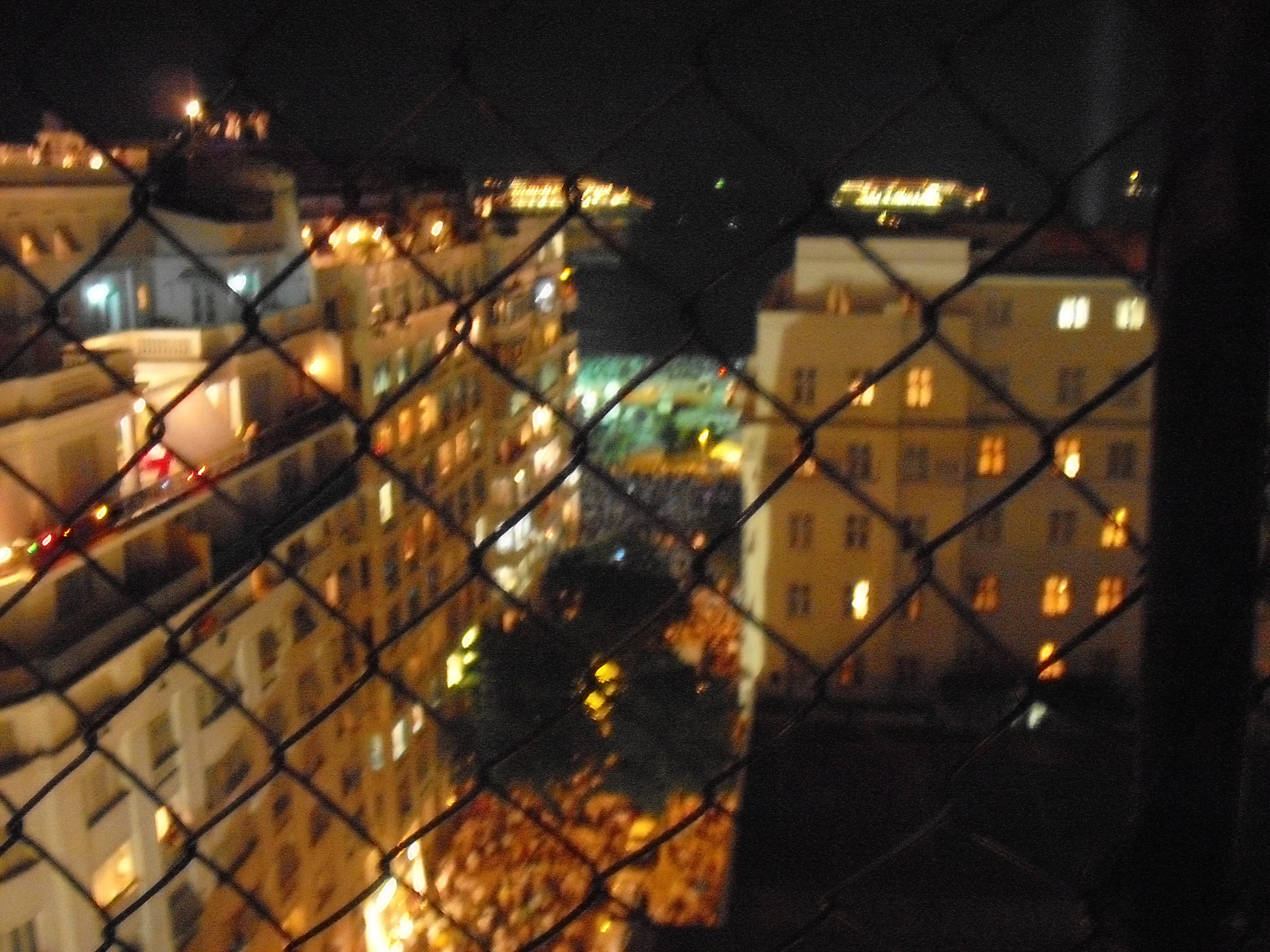 an image of night time city from behind a chain link fence