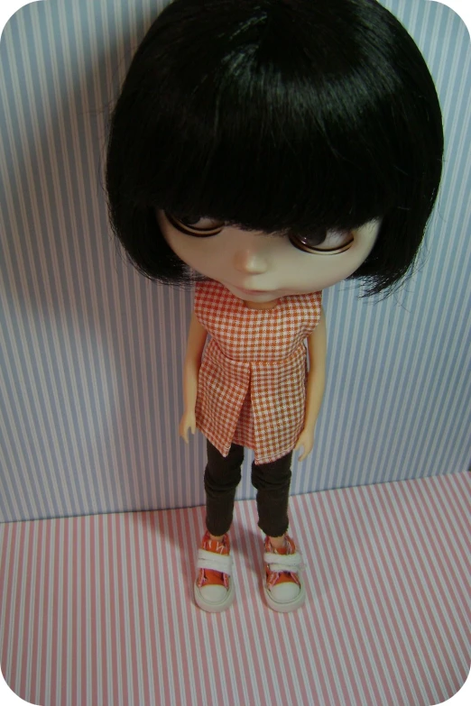 a small doll with short black hair and plaid dress is standing