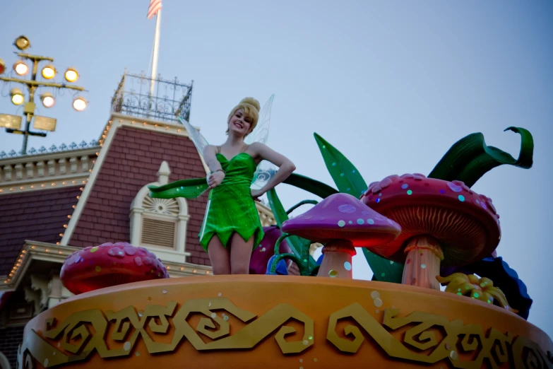 the young woman in the green dress is standing on top of a mushroom sculpture