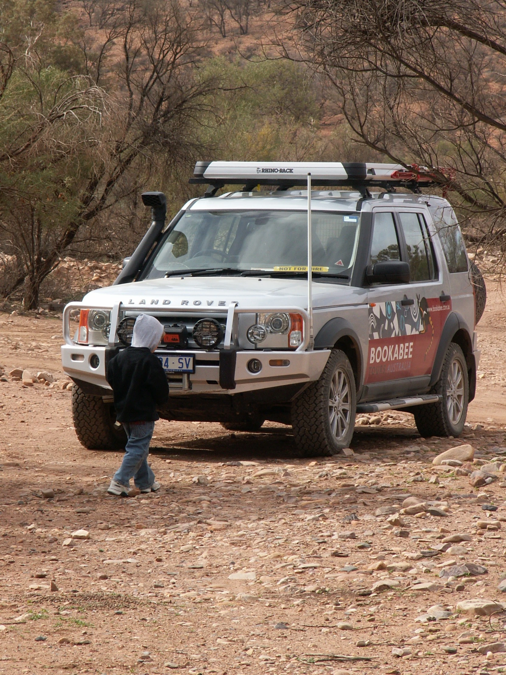 a man is in front of a silver vehicle in a dirt field