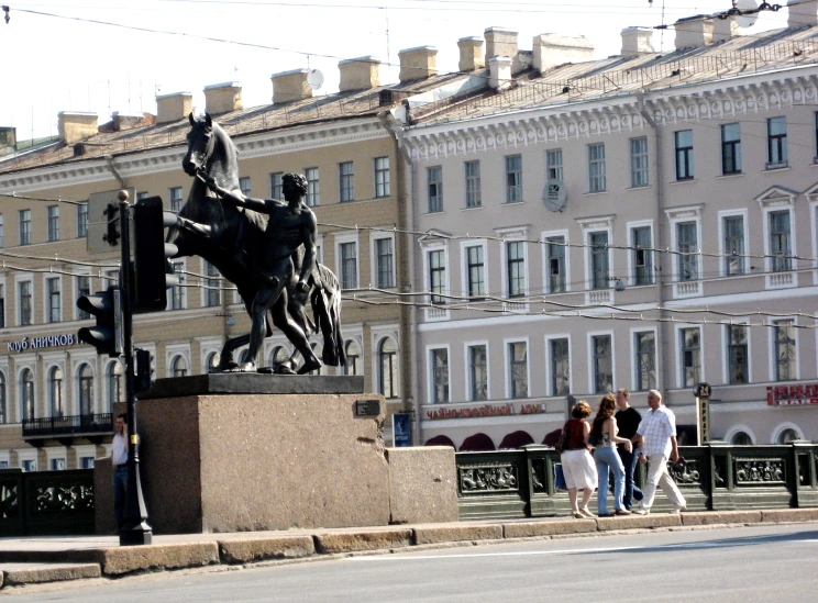 several people walking near a statue in front of several apartment buildings