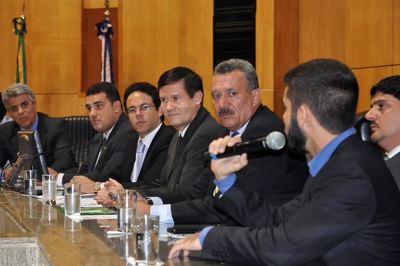 five men sitting at a long table with microphones