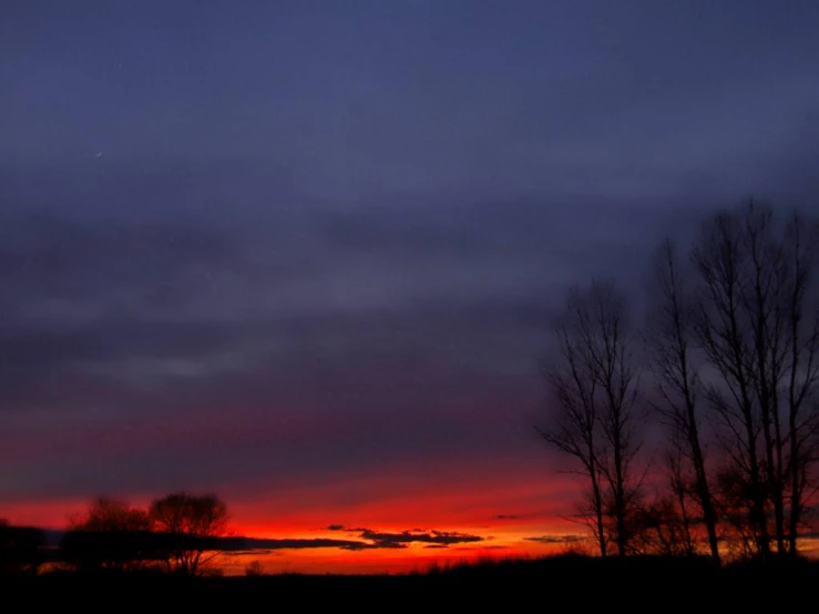 the sun is setting in the sky over some trees