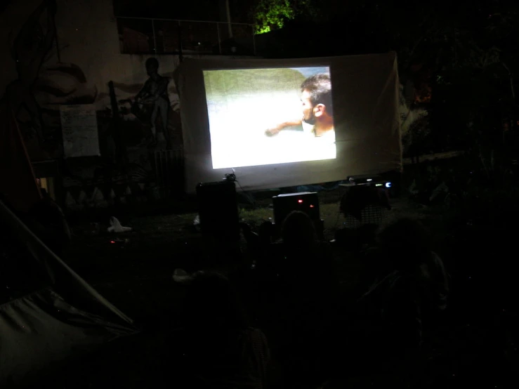 people sitting in a field watching a movie on a large screen