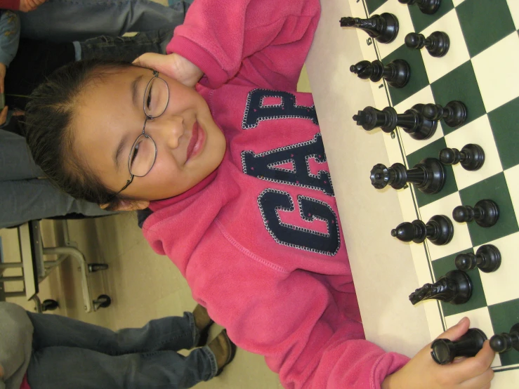 a girl is sitting at the table next to a chess board