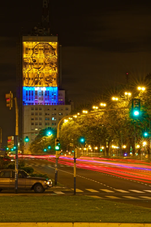 cars passing a city street at night with a large building in the background