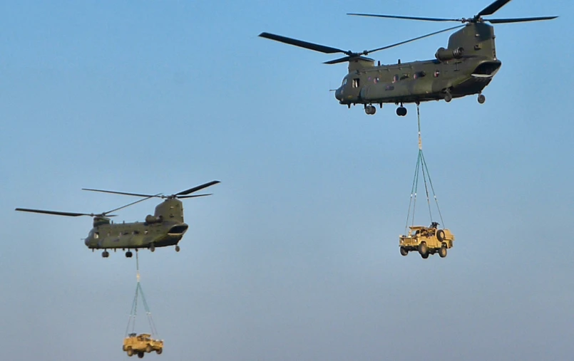 military vehicles being hoisted by three crane lifters