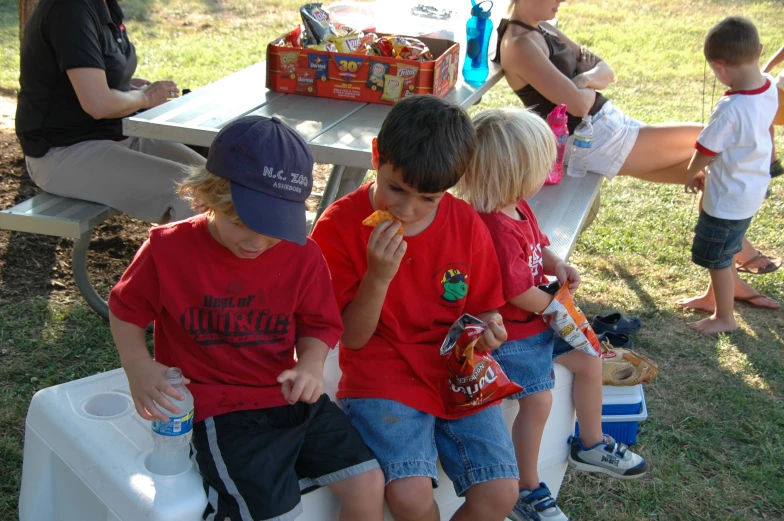 two children eating  dogs while people eat snacks behind them