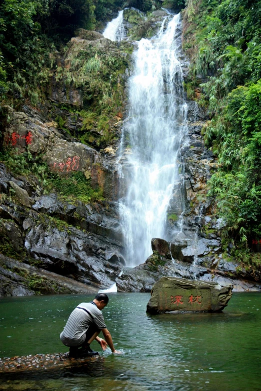 a man kneeling in front of a waterfall