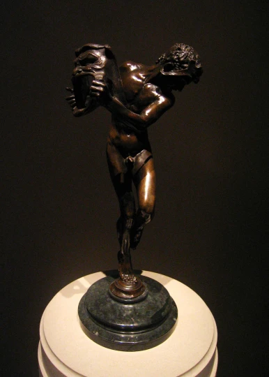 a bronze figurine is holding a snake on top of a round object