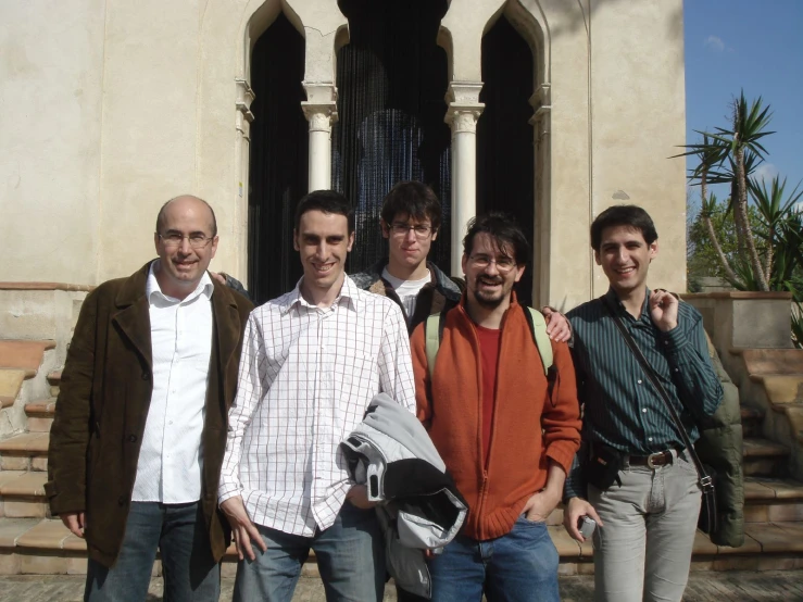 four men smiling for the camera while standing in front of a building