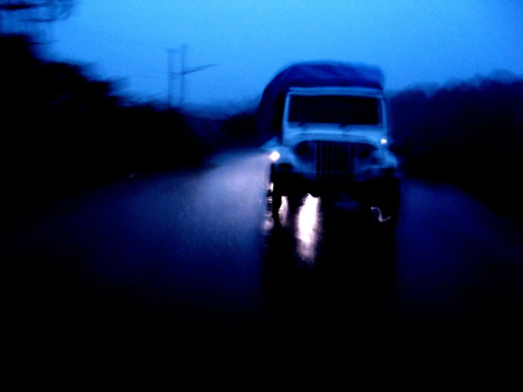 an old truck driving down a wet street in the rain