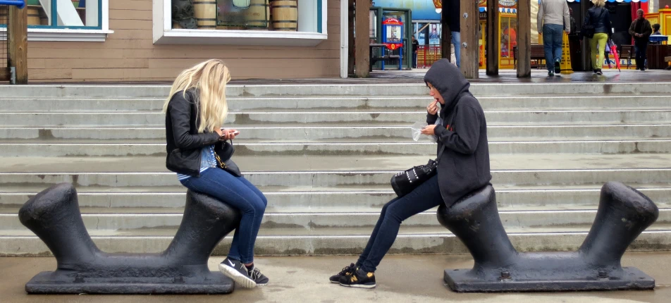 two women sit on giant foot steps talking on their phones