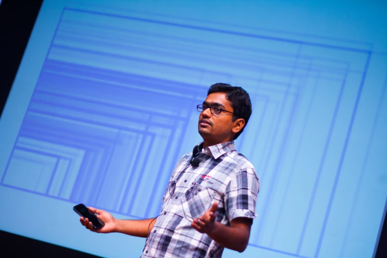 a man speaking on stage while holding onto a cell phone