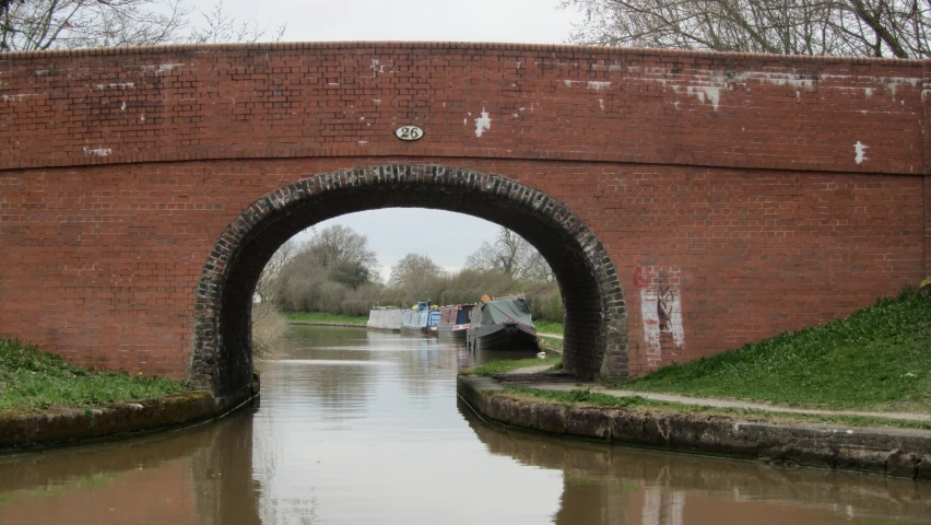 a canal with two boats passing under a brick bridge