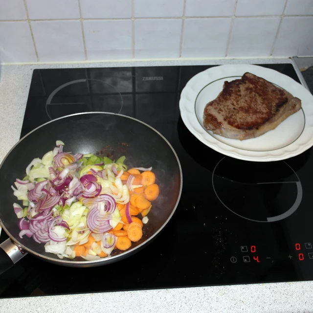 a pan with meat, onions and carrots cooking on the stove