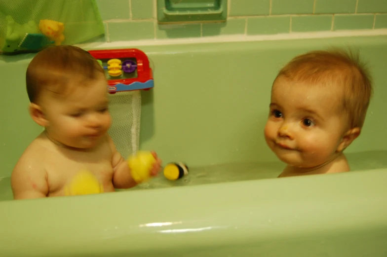 two babies playing in a bath tub with toys