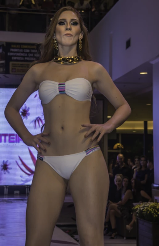 a beautiful young woman in a white bikini and high heels standing next to a crowd