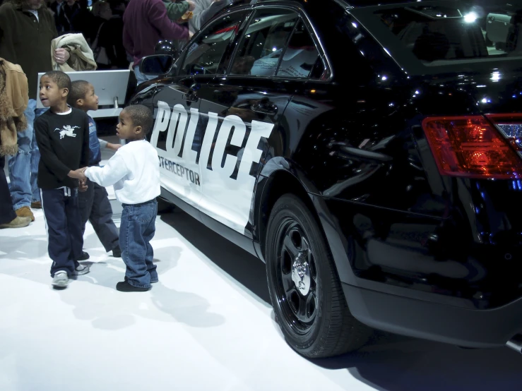 two little boys standing next to a police car