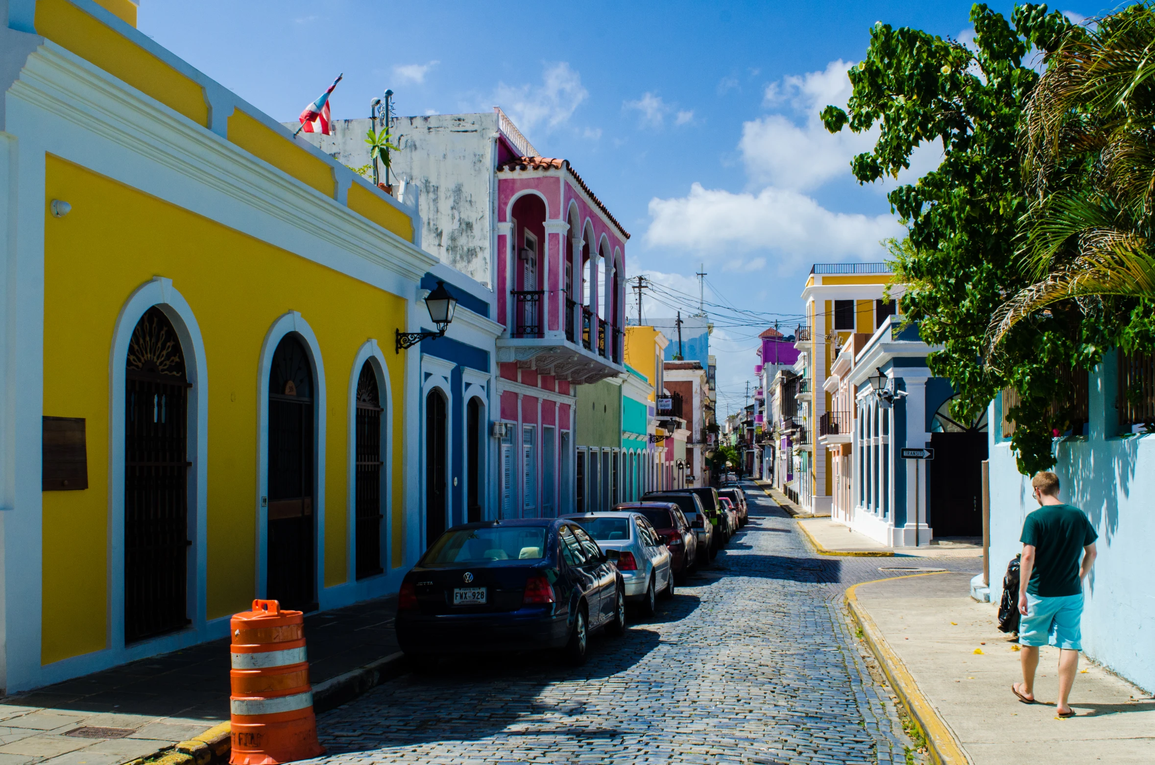 a small street lined with parked cars with people walking on the sidewalk