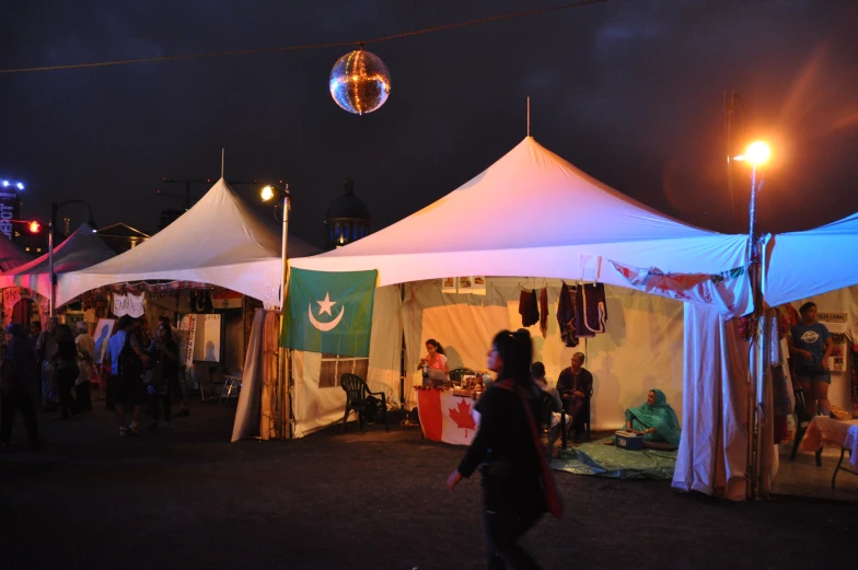 people sitting outside tents with some lights and signs