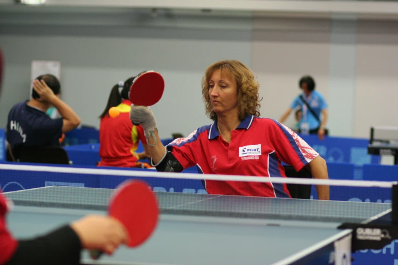 a woman standing at a ping pong table with two people watching