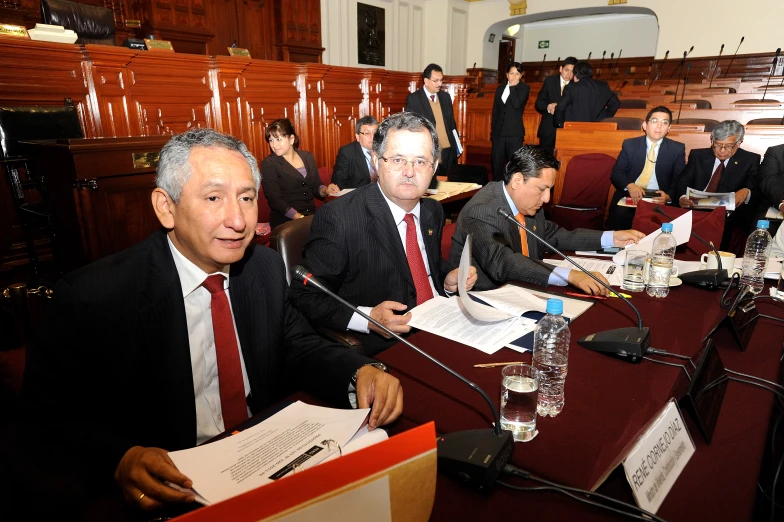 several men in suits are sitting at a long desk