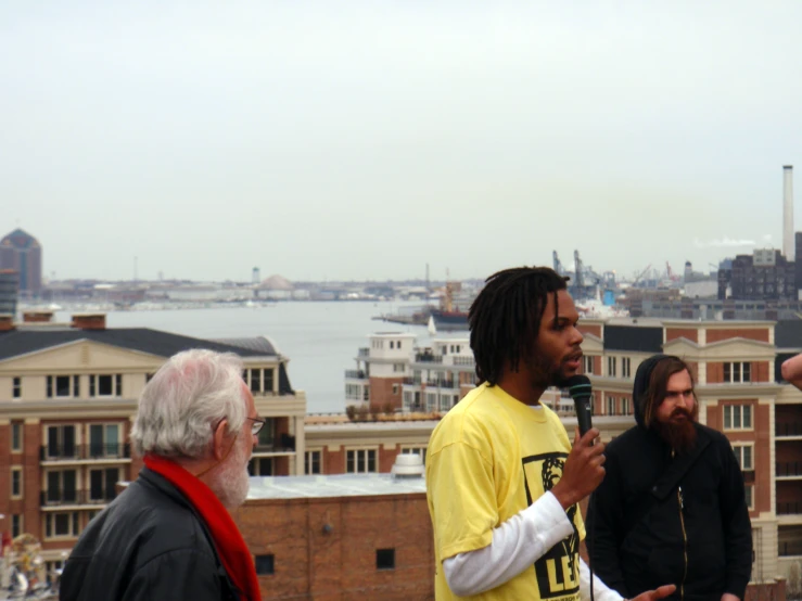 a man with dreadlocks talking into microphone standing in front of other people