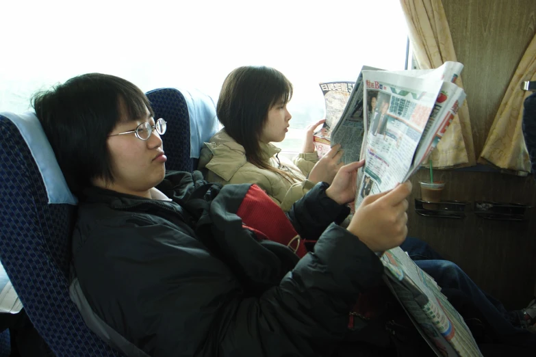 two people reading newspapers on an airplane