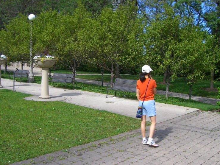 an adult man in an orange shirt and blue shorts is walking down a paved path