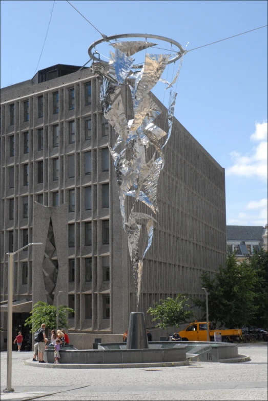 people walk past a large sculpture in front of a building