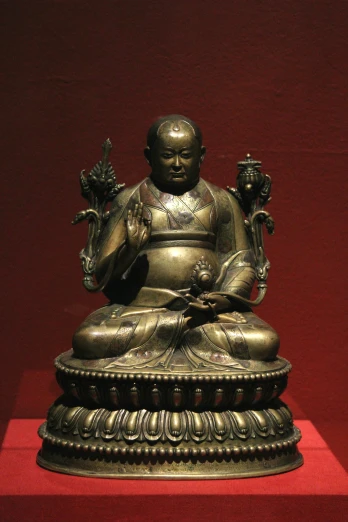 a bronze buddha statue sitting on top of a red stand