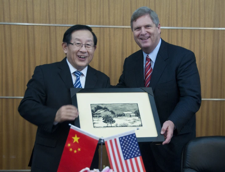 two asian men holding american and chinese flags