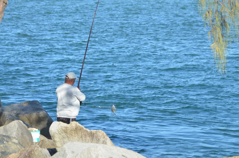 a man fishing in the water from a rock with a fishing pole