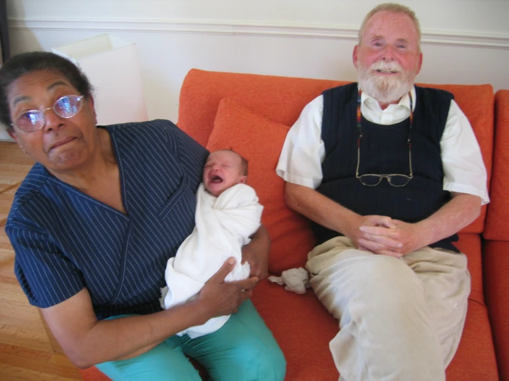 a woman holding her baby in the arms of an older man on a couch