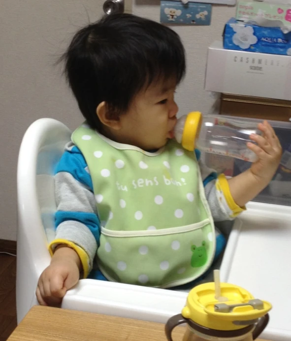 small child with green bib drinking out of a water bottle