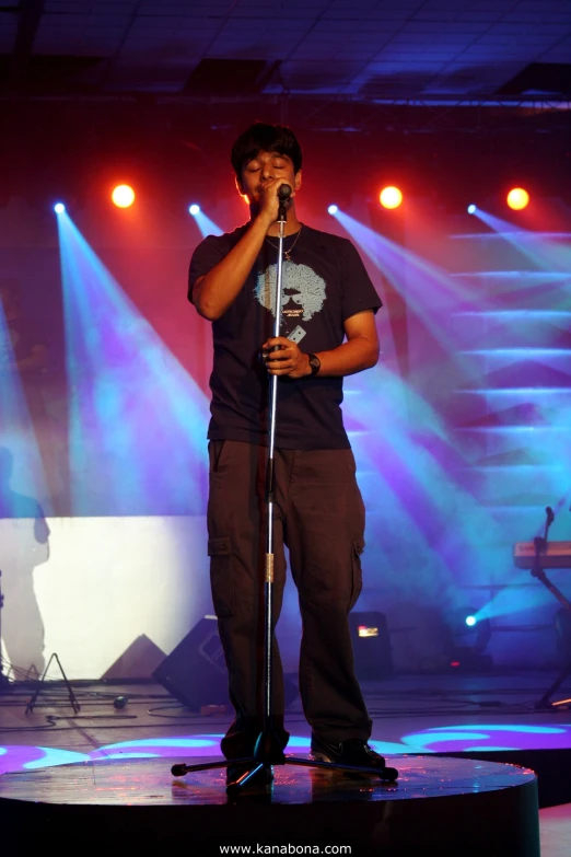 man holding microphone on stage with spotlights on a purple and blue background