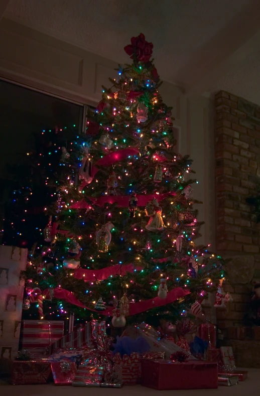 a brightly lit christmas tree stands in front of a brick wall