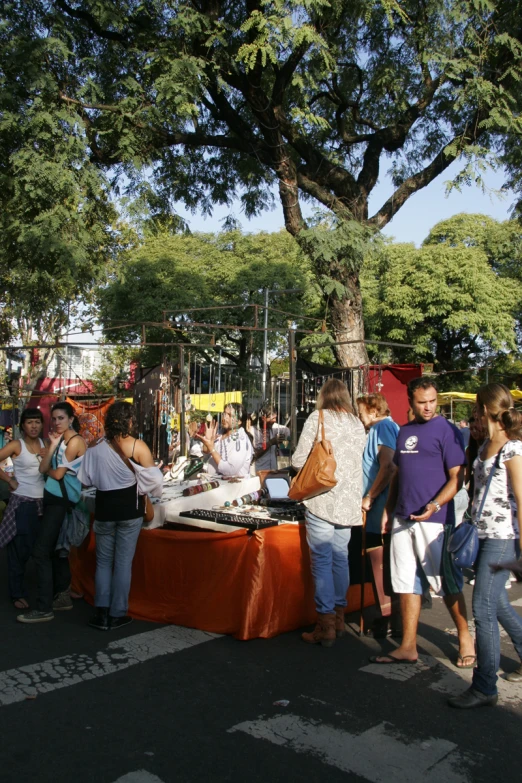 people are standing near a food stand under the shade of trees