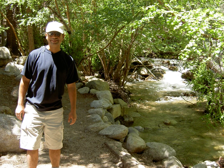 a man smiles and stands next to a stream