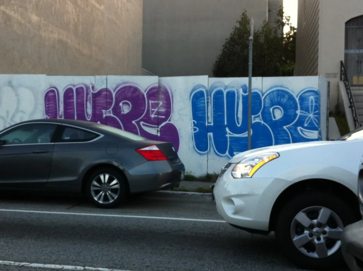 two cars parked next to each other in front of a white wall covered with graffiti