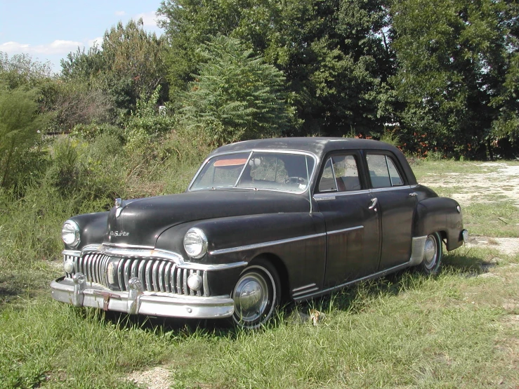 an old black car sitting in the grass near trees