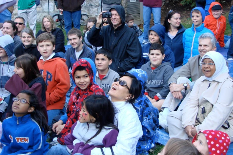 a crowd of s sitting on a hill while people take pos