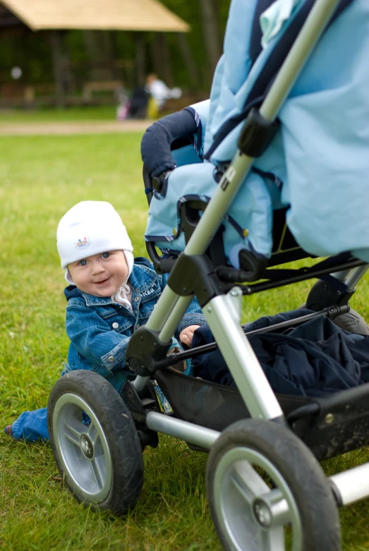 a toddler sitting in the grass near an infant stroller