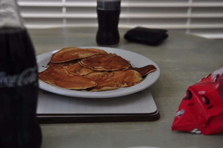 a white plate with pancakes and soda on a table