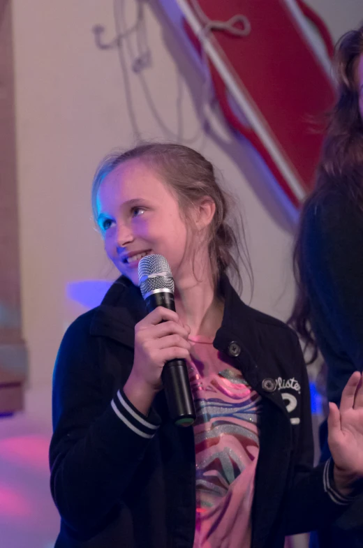 a girl talking into a microphone while two other girls stand behind her